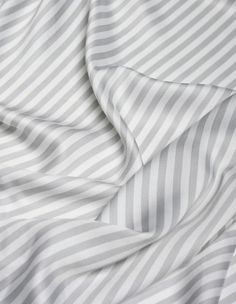 The Cozy Earth Bamboo Flat Sheet features a white fabric with diagonal light gray stripes that drape softly, forming gentle folds and shadows. The consistent pattern and smooth, silky texture enhance its luxurious feel.