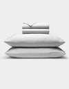 Two stacked pillows with subtle gray and white stripes are shown beneath a neatly folded Cozy Earth Bamboo Sheet Set, all displayed against a plain white background.|Color:Classic Stripe in Dew