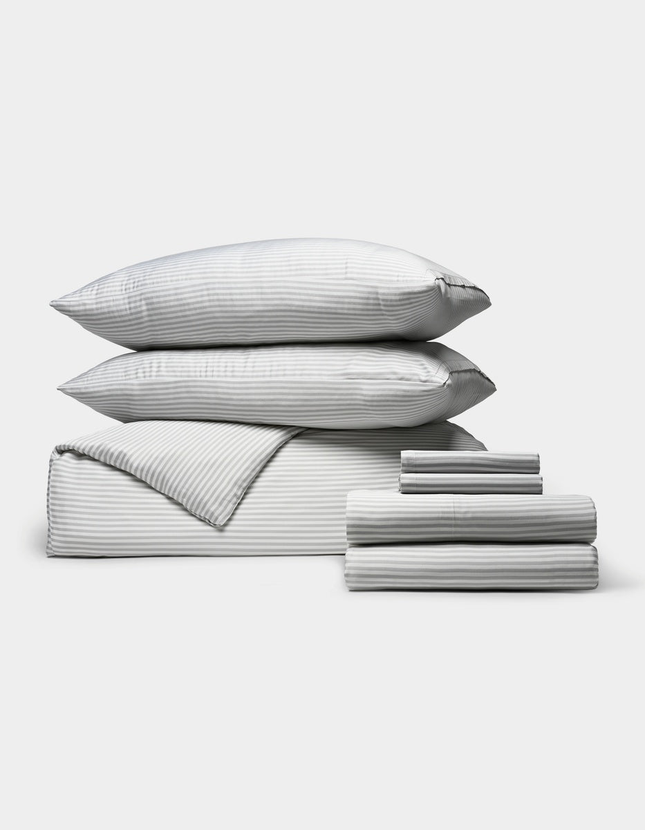 A neatly stacked set of Cozy Earth’s Bamboo Bedding Ultimate Bundle, featuring two pillows, a folded comforter, and two stacks of folded sheets in gray and white stripes, displayed on a light gray background.|Color:Classic Stripe in Dew