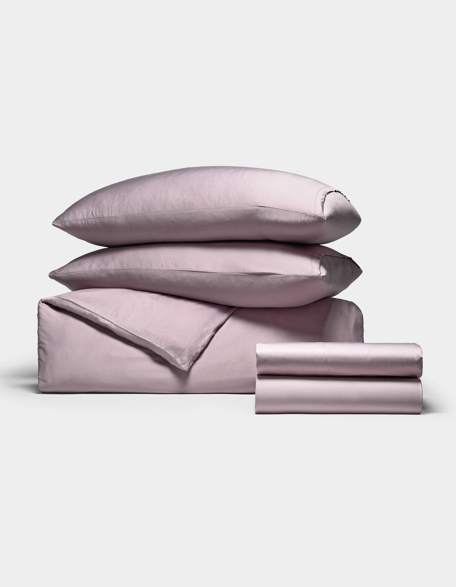 The Cozy Earth Bamboo Bedding Deluxe Bundle, in lavender, includes two pillows, a duvet, and sheets neatly folded and displayed on a plain white background.|Color:Lavender