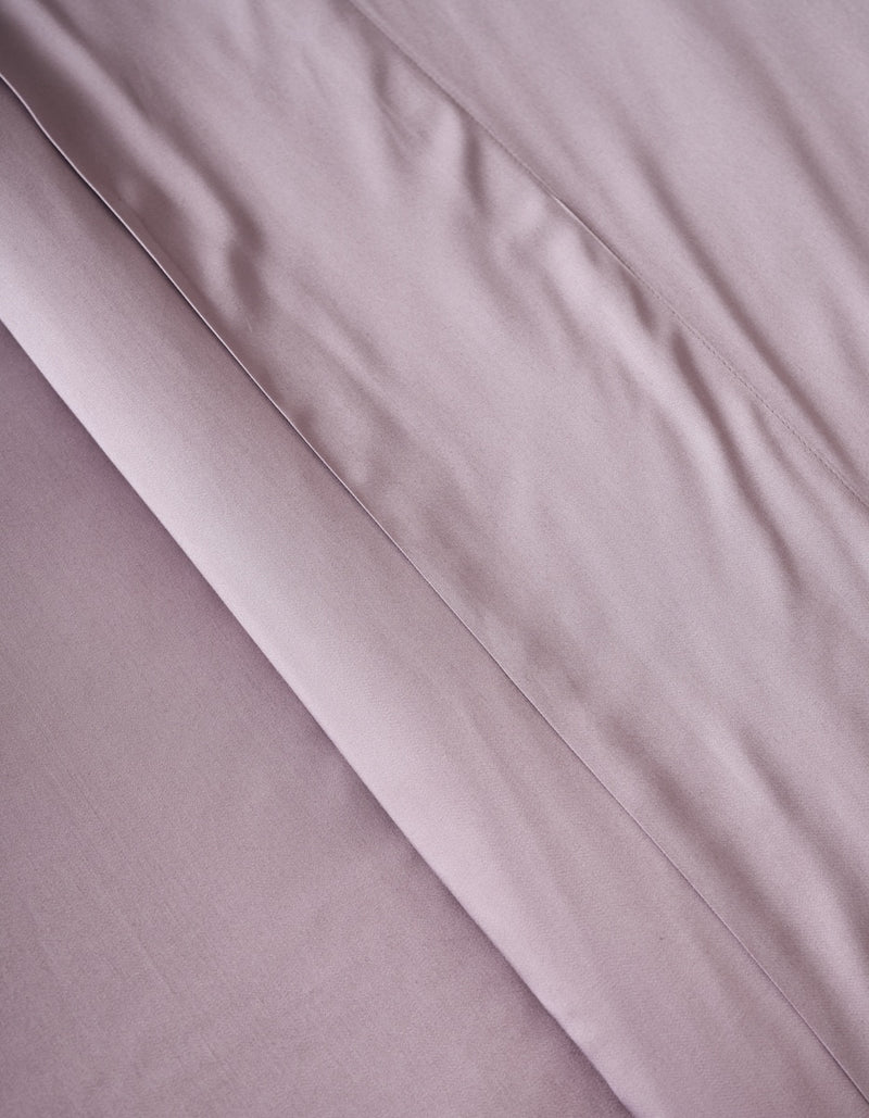 A close-up of the Cozy Earth Bamboo Duvet Cover in soft, light mauve shows visible folds and creases that create gentle shadows and enhance its textured appearance.