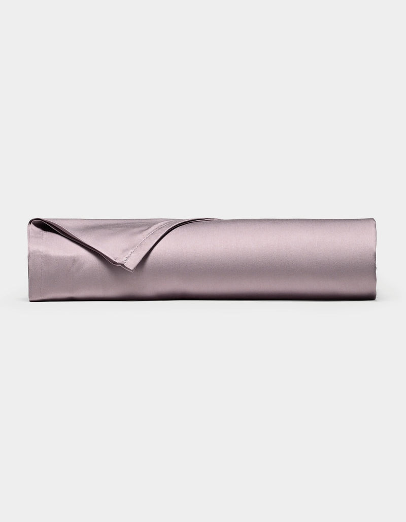 A neatly rolled, lavender-colored Bamboo Flat Sheet by Cozy Earth, with one corner folded over, displayed against a plain white background.