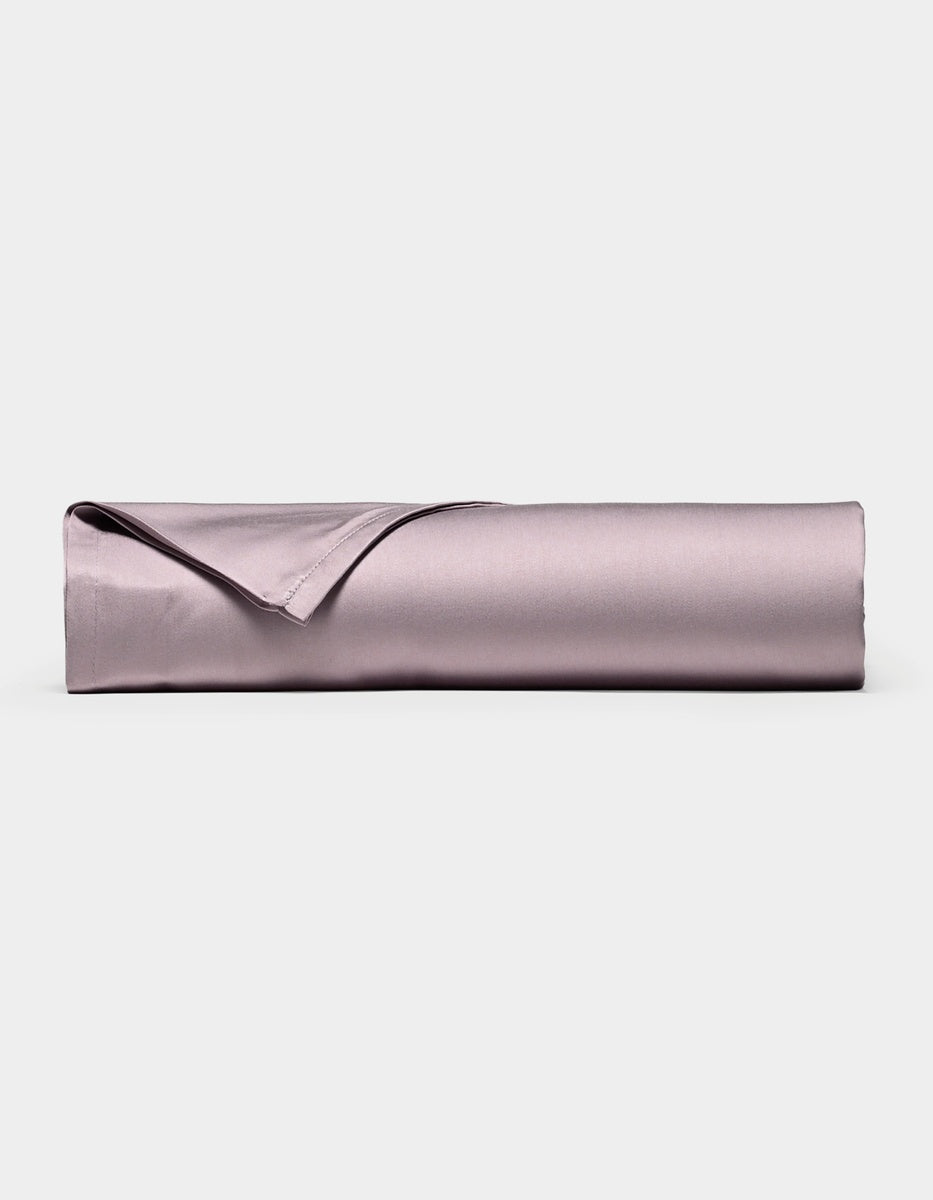 A neatly rolled, lavender-colored Bamboo Flat Sheet by Cozy Earth, with one corner folded over, displayed against a plain white background.|Color:Lavender