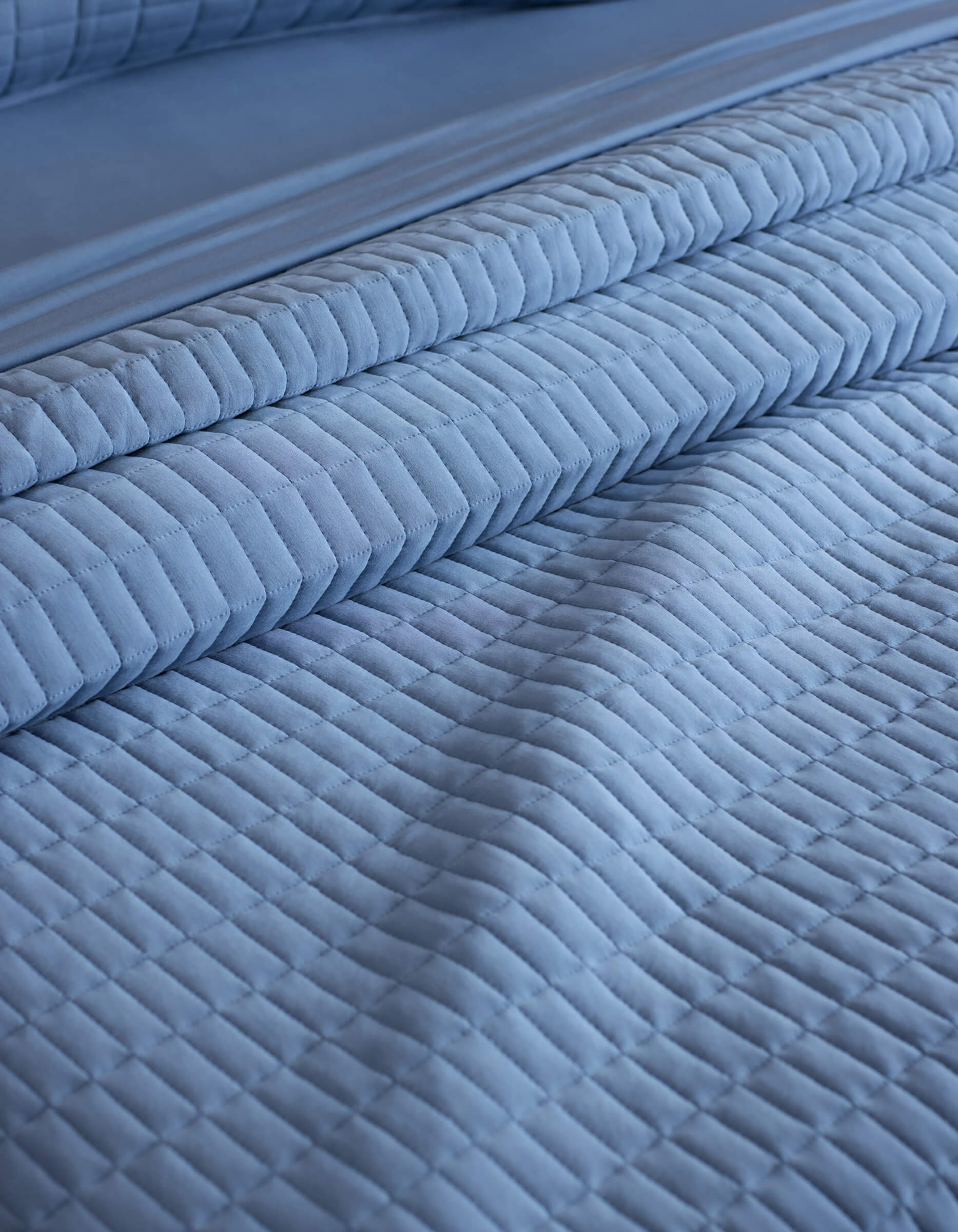 Close-up of a neatly made bed with the Cozy Earth Bamboo Jersey Quilt in light blue, featuring a quilted grid pattern and matching pillowcases. The soft, textured fabric creates an inviting look.
