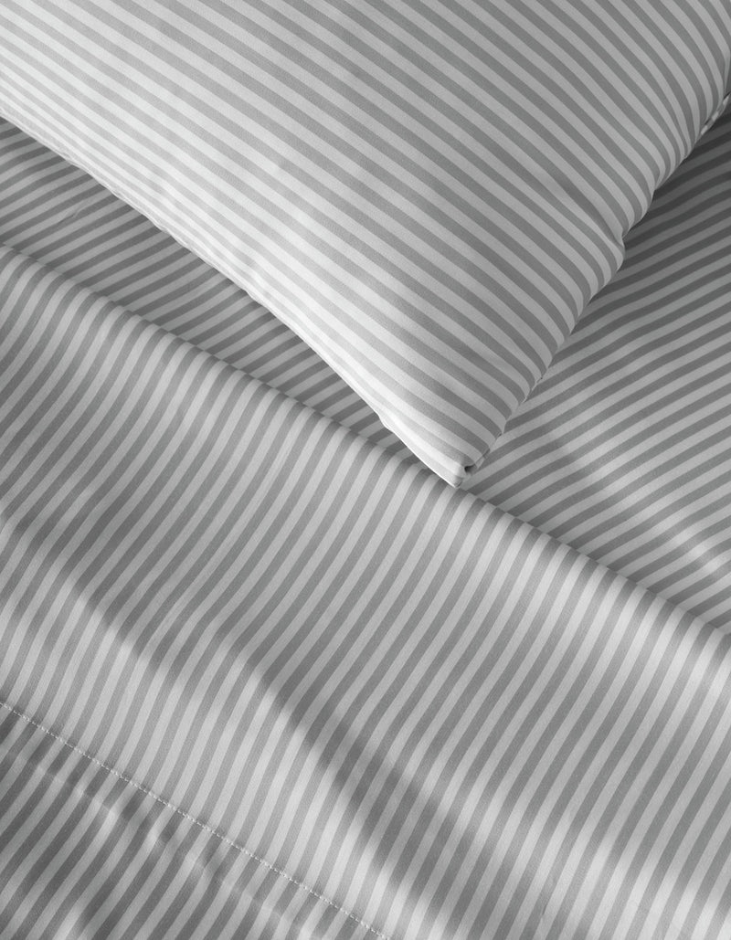 Close-up of a bed with a pillow and sheets featuring the Bamboo Flat Sheet from Cozy Earth in a gray and white diagonal stripe pattern.