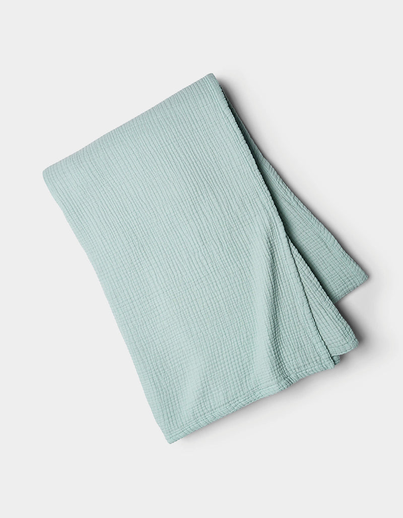 The Cozy Earth Cotton Gauze Blanket, in light blue with a textured finish, is neatly folded and displayed on a plain white background.