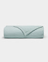 The Cozy Earth Cotton Gauze Blanket is neatly folded in light blue with a textured, grid-like pattern on a plain white background. One corner is turned down to reveal the inner side.|Color:Tide