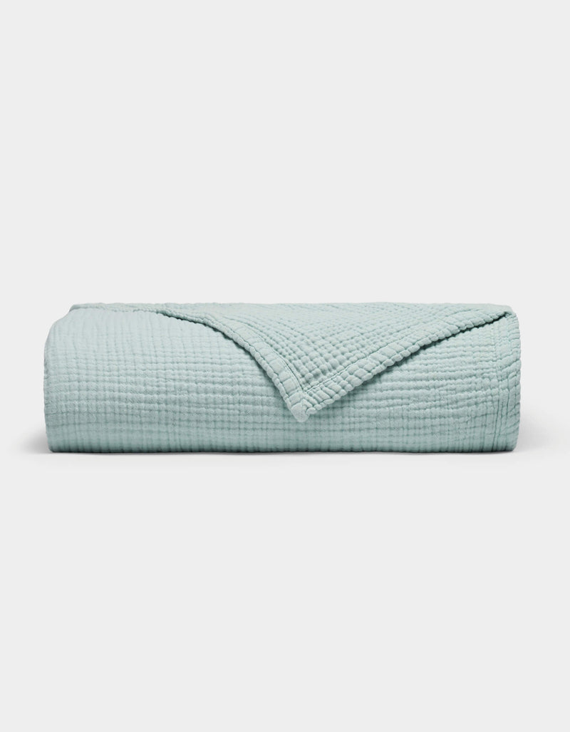 The Cozy Earth Cotton Gauze Blanket is neatly folded in light blue with a textured, grid-like pattern on a plain white background. One corner is turned down to reveal the inner side.