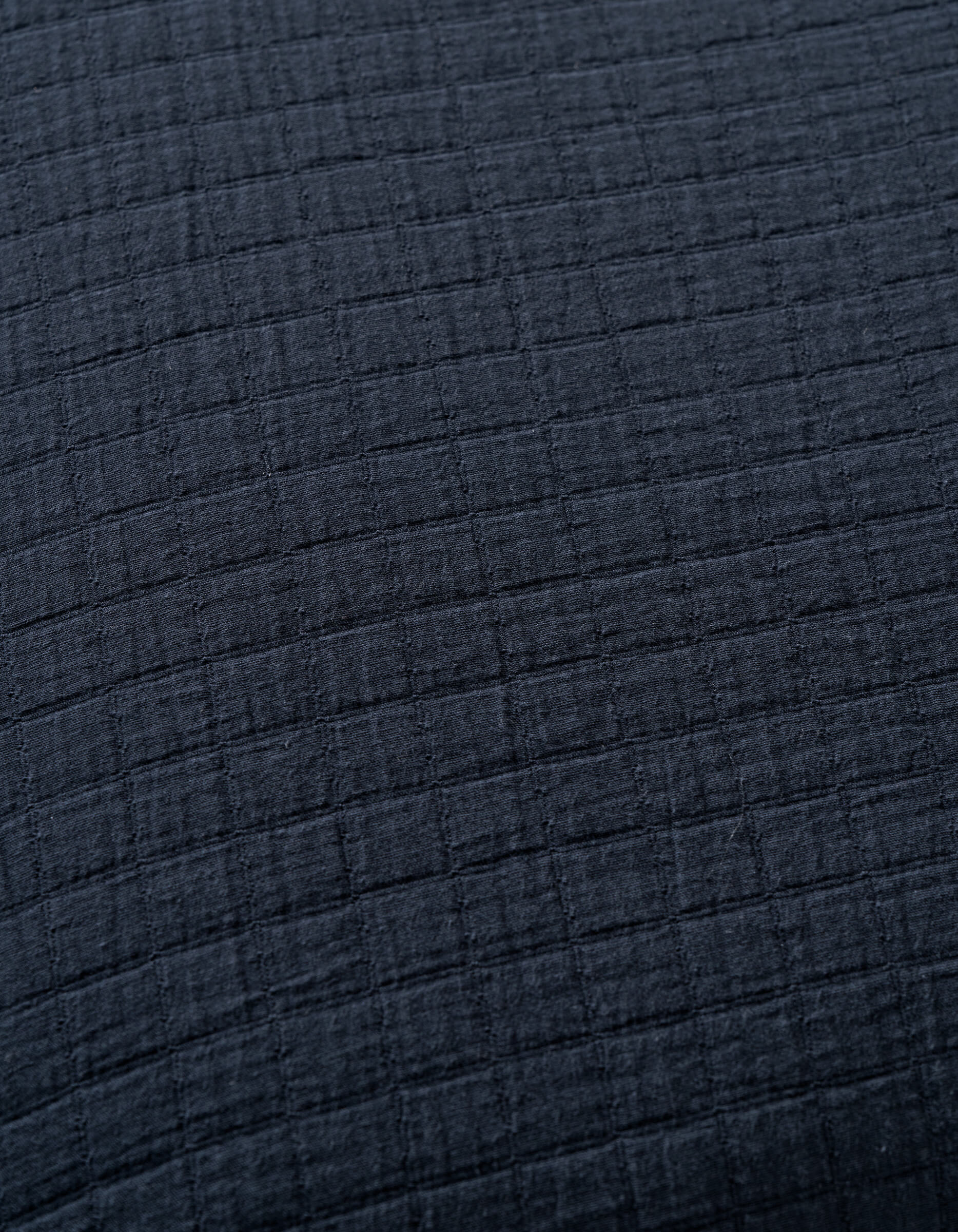 Close-up of Cozy Earth's Waterfront Grid Matelasse Blanket in dark gray or black, featuring a soft textured fabric with a subtle grid pattern formed by raised horizontal and vertical lines.