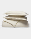The Cozy Earth Linen Duvet Set features cream-colored, soft and smooth bedding—two pillows stacked atop a folded duvet—displayed against a plain white background.