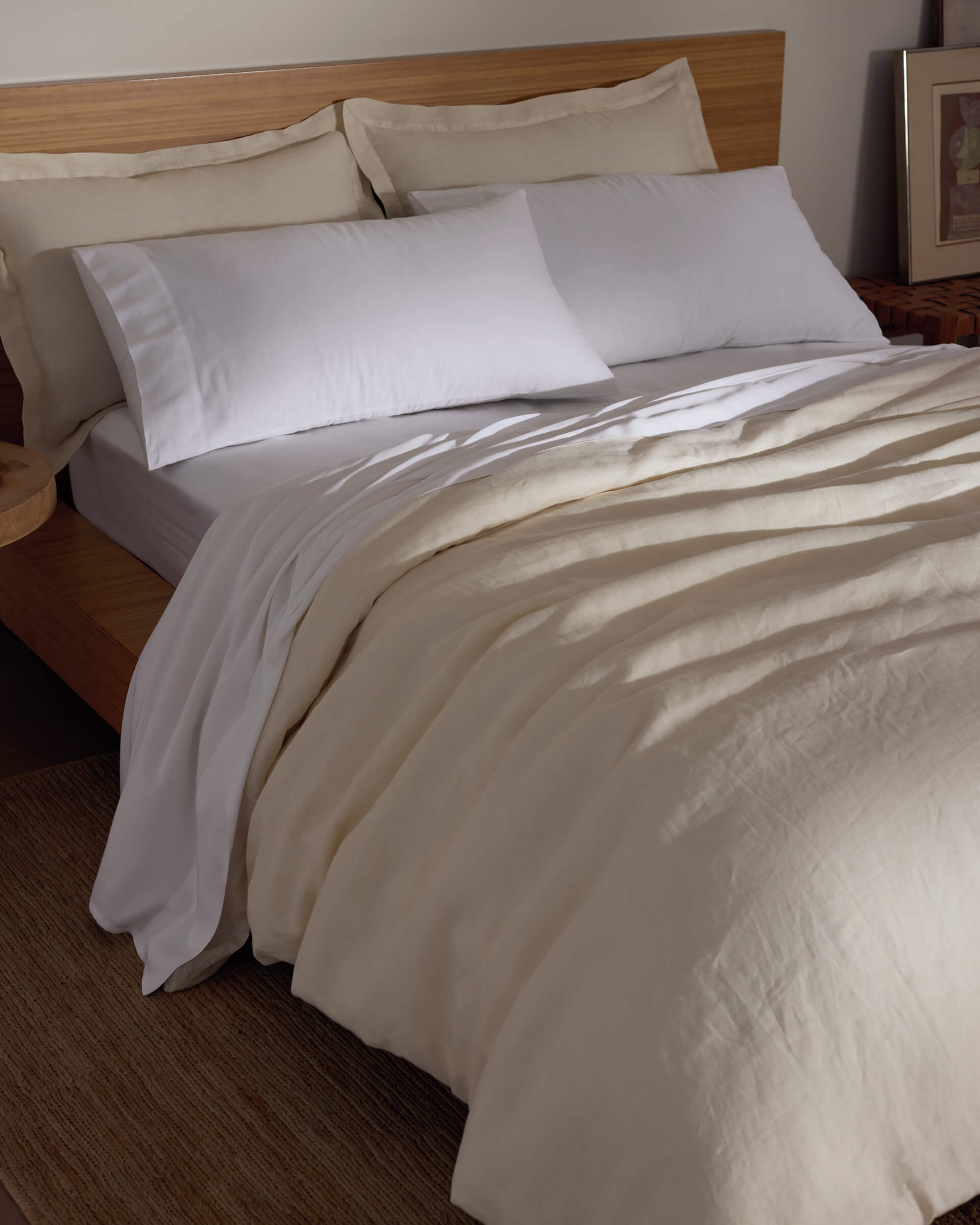 A bed features the Cozy Earth Linen Duvet Cover, white pillows, and a wooden headboard. A bedside table adds warmth to the softly lit room, creating a cozy and inviting atmosphere.|Color:Flax
