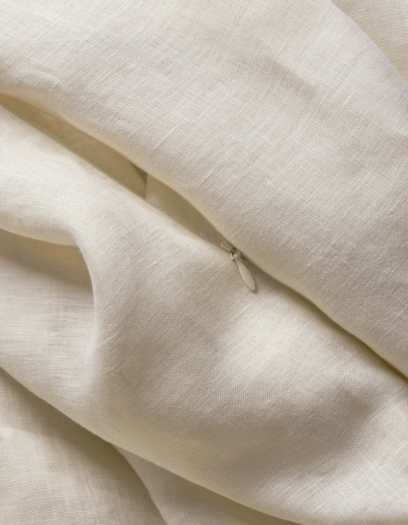 A cream-colored Cozy Earth Linen Duvet Cover with a textured weave is softly draped and folded, revealing a small, partially visible metal zipper pull among the folds.
