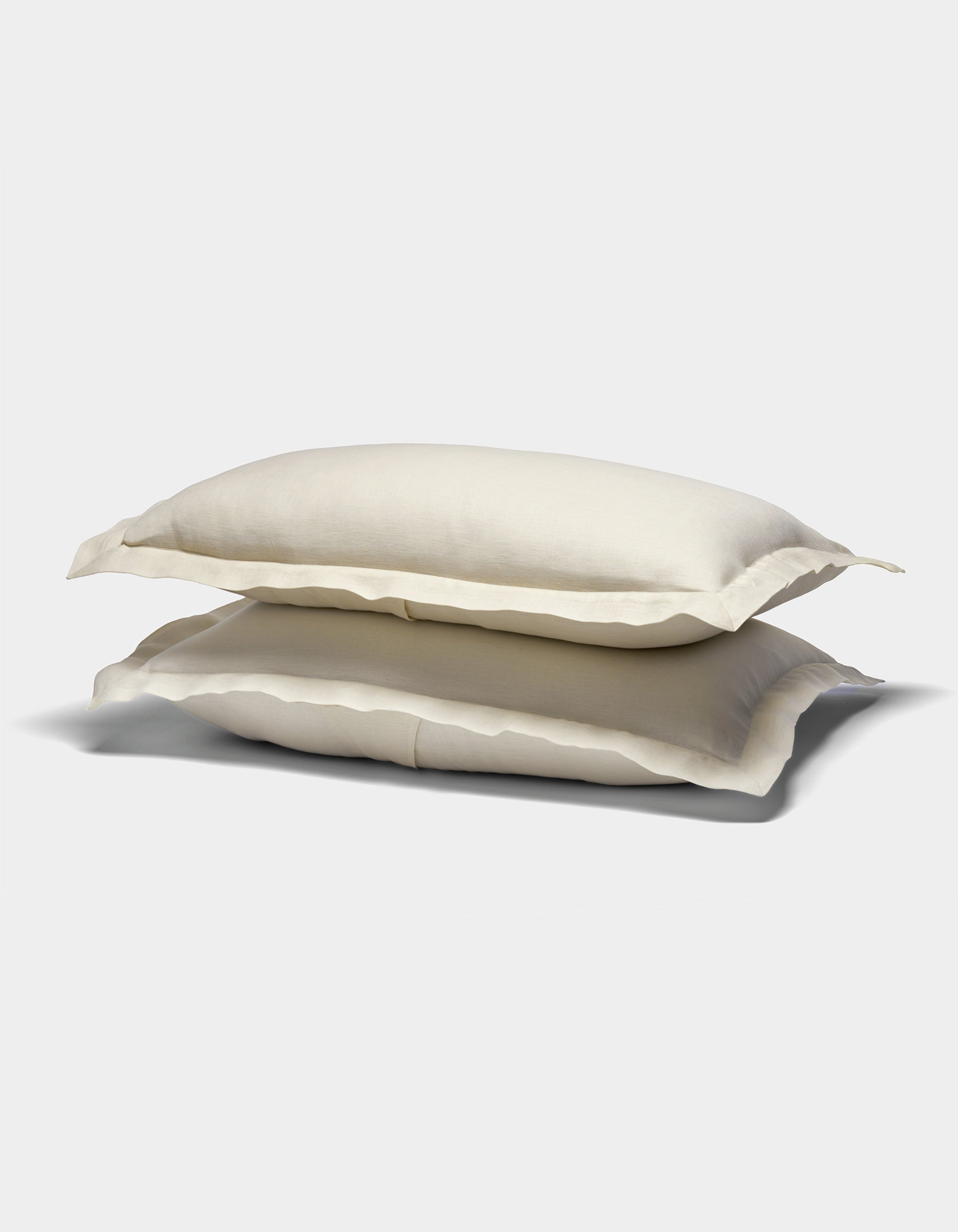 Two cream-colored Cozy Earth Linen Shams with slightly ruffled edges are stacked on top of each other against a plain white background.