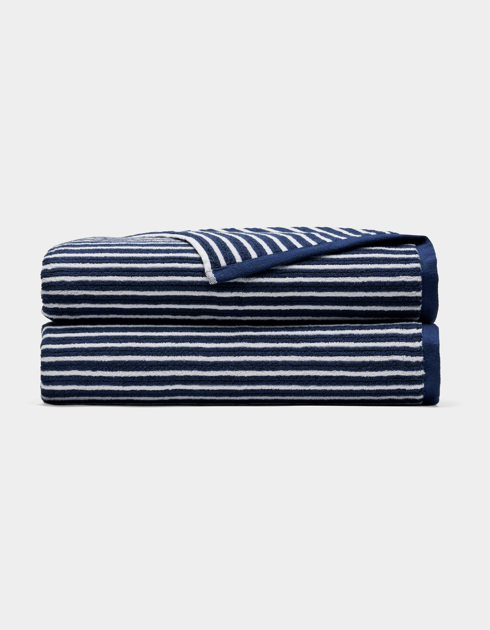 A Cozy Earth Ribbed Terry Bath Sheet in navy blue with horizontal white stripes, neatly folded and stacked on a plain light background.