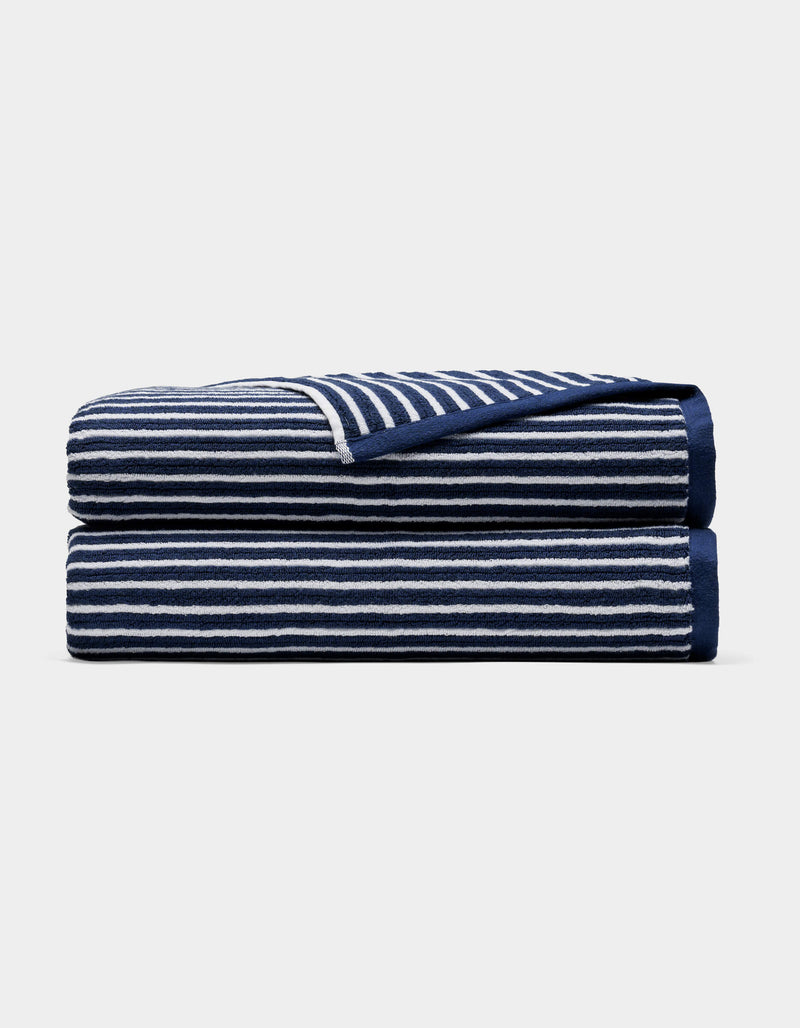 A Cozy Earth Ribbed Terry Bath Sheet in navy blue with horizontal white stripes, neatly folded and stacked on a plain light background.