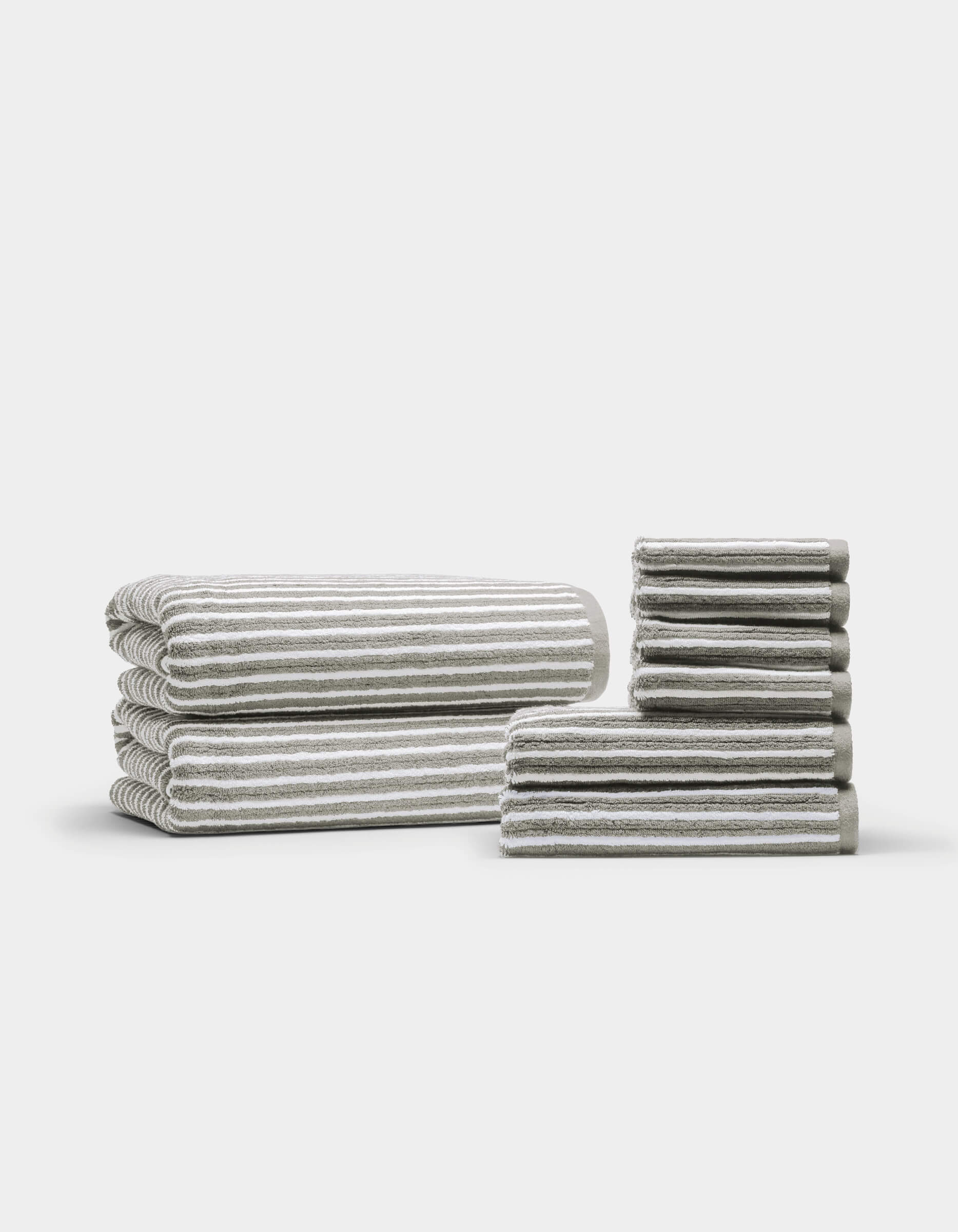 Two neatly arranged stacks of the Cozy Earth Ribbed Terry Bath Towel Set are displayed on a plain white background—one larger stack featuring bath towels, and a smaller stack showcasing hand towels and washcloths.