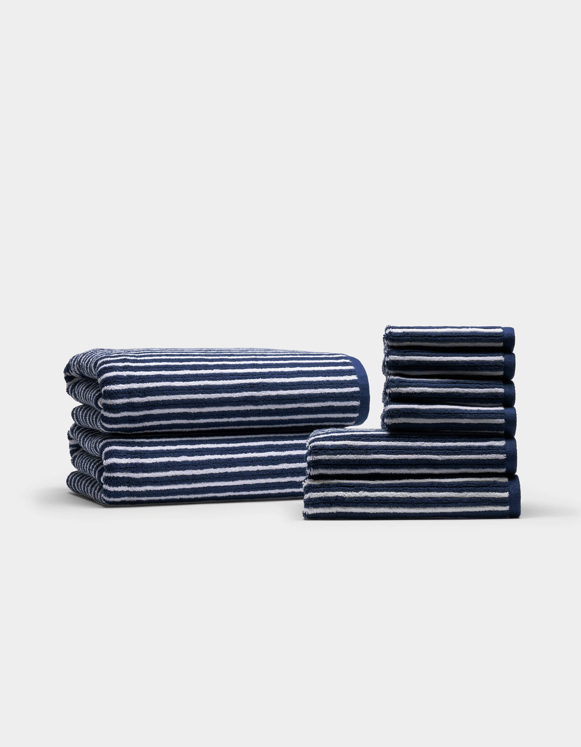 Cozy Earth's Ribbed Terry Bath Towel Set, featuring neatly folded navy blue and white striped towels, is stacked in two organized piles against a plain light background. The towels are arranged by size, creating even and orderly stacks.
