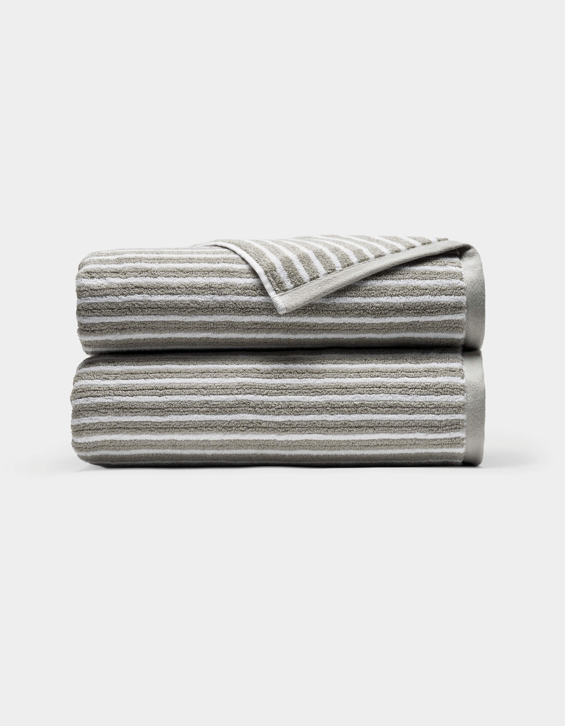 Two neatly folded Ribbed Terry Bath Towels by Cozy Earth, light gray with horizontal white stripes, stacked atop each other against a plain white background. A corner of the top towel is turned over, revealing the underside.