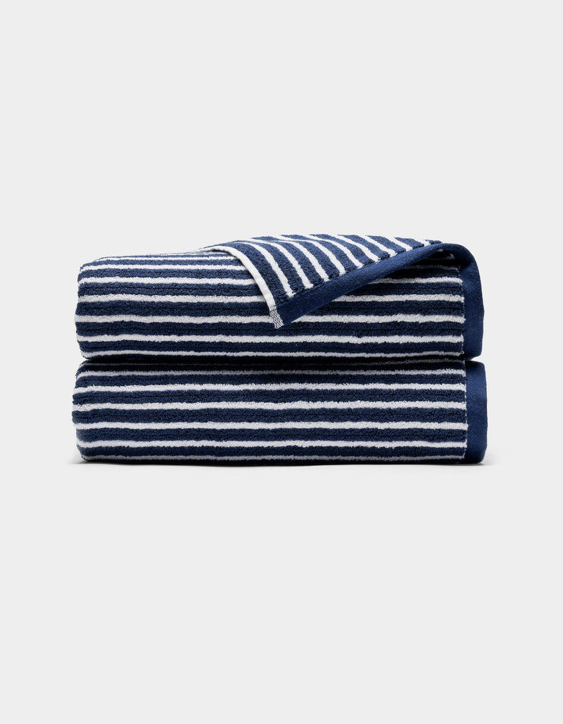 A Ribbed Terry Bath Towel by Cozy Earth, navy blue with white horizontal stripes, is neatly folded and displayed on a light gray background.