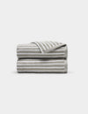 Two Ribbed Terry Hand Towels by Cozy Earth, in beige and white stripes, stacked neatly with one corner of the top towel flipped to show the stripe pattern, set against a plain white background.|Color:Dew Stripe