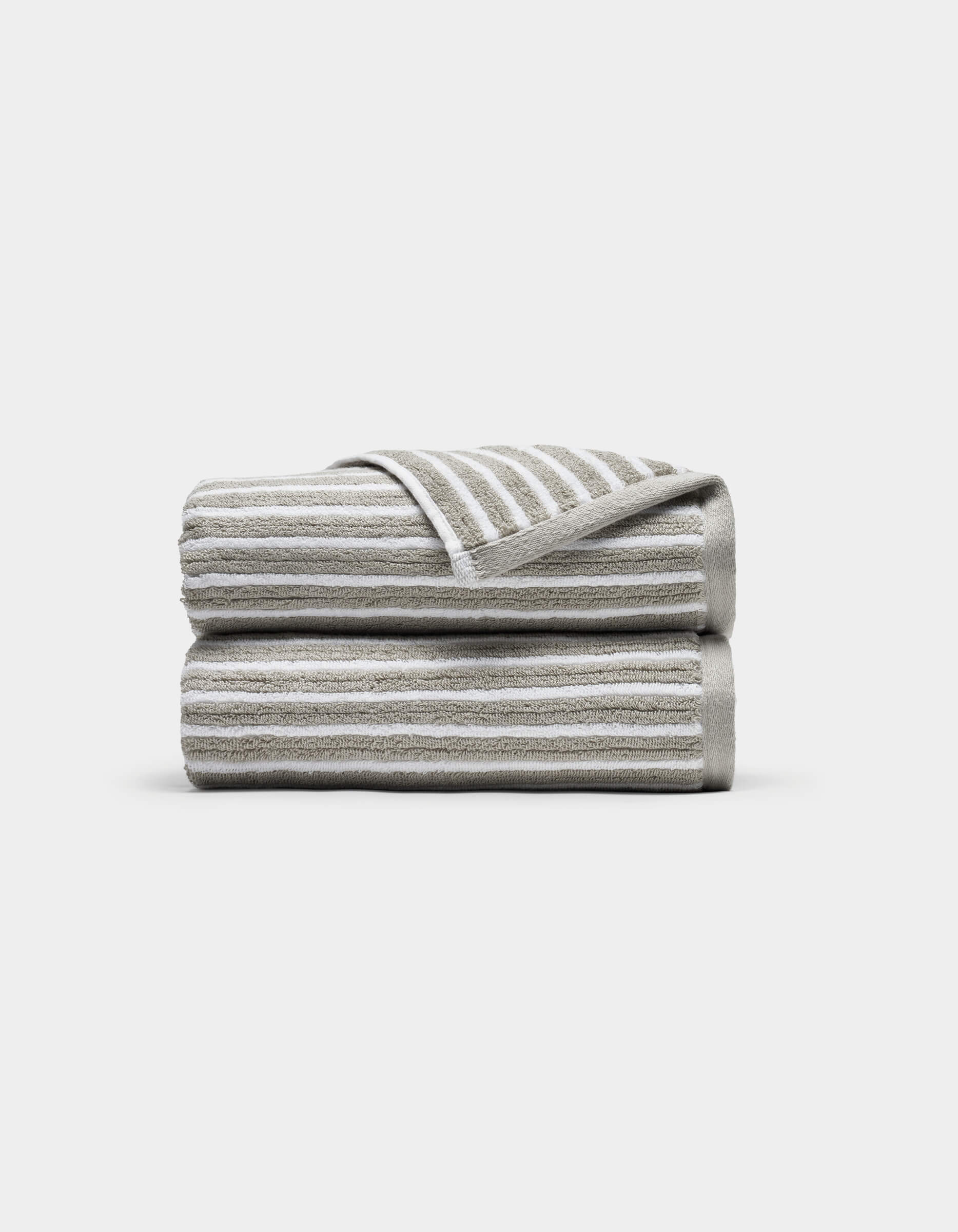 Two Ribbed Terry Hand Towels by Cozy Earth, in beige and white stripes, stacked neatly with one corner of the top towel flipped to show the stripe pattern, set against a plain white background.