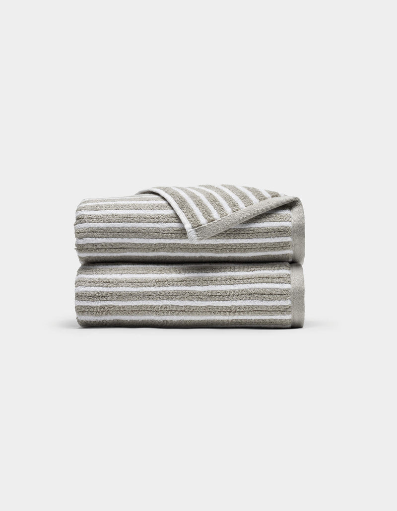 Two Ribbed Terry Hand Towels by Cozy Earth, in beige and white stripes, stacked neatly with one corner of the top towel flipped to show the stripe pattern, set against a plain white background.