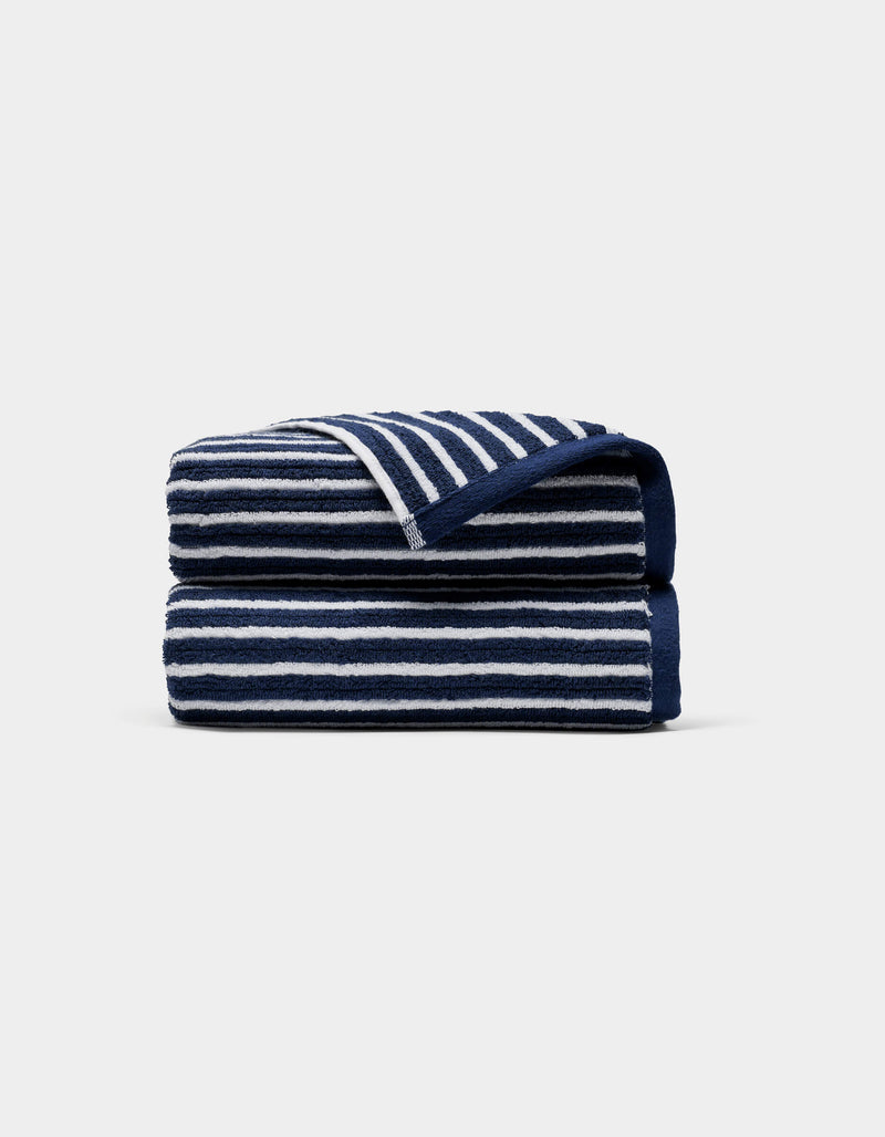 A Ribbed Terry Hand Towel by Cozy Earth, featuring horizontal navy blue and white stripes, is neatly folded against a plain light gray background.