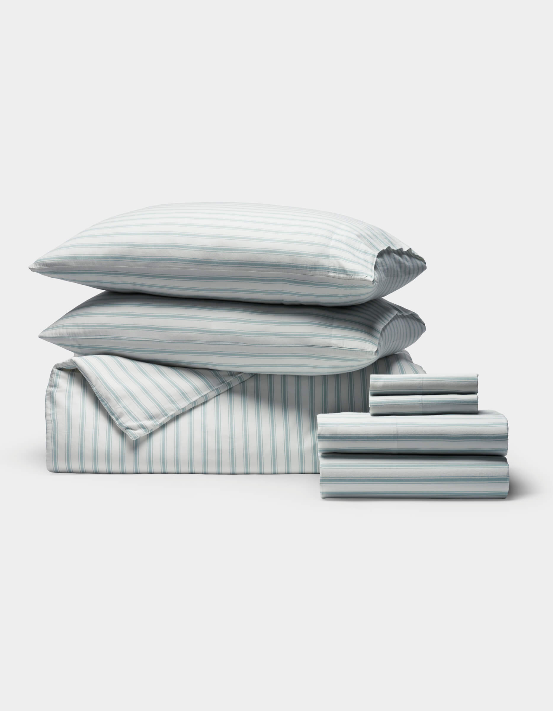 A neatly arranged stack of Cozy Earth's Soft-Wash Cotton Bedding Core Bundle, including pillows, a comforter, and folded sheets in white and light blue, displayed on a plain white background.|Color:River and Sea Salt Stripe