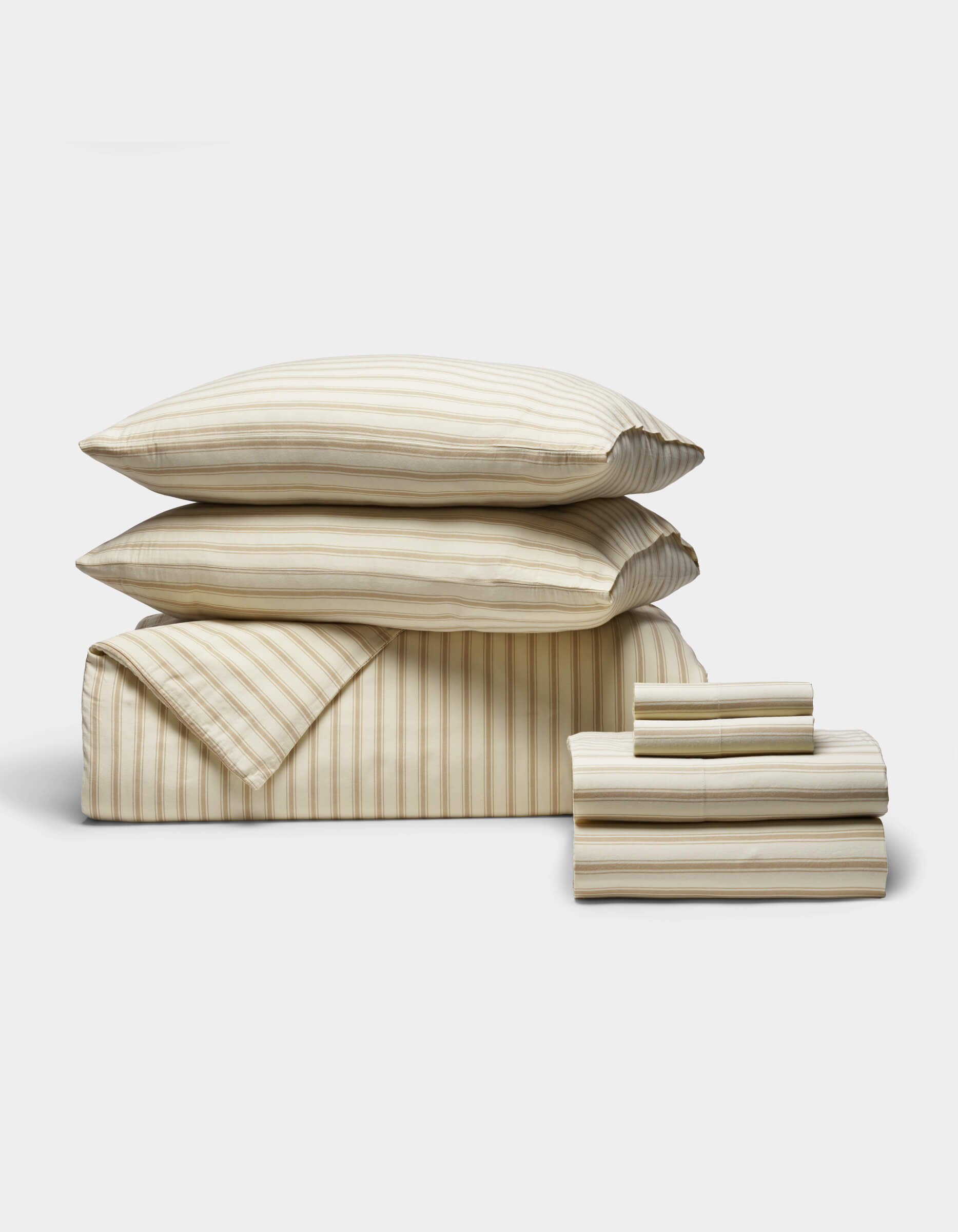 The Soft-Wash Cotton Bedding Core Bundle by Cozy Earth features cream and beige striped bedding with two stacked pillows, a folded comforter, and a neatly folded sheet stack, all displayed against a plain white background.|Color:Coconut and Sandalwood Stripe