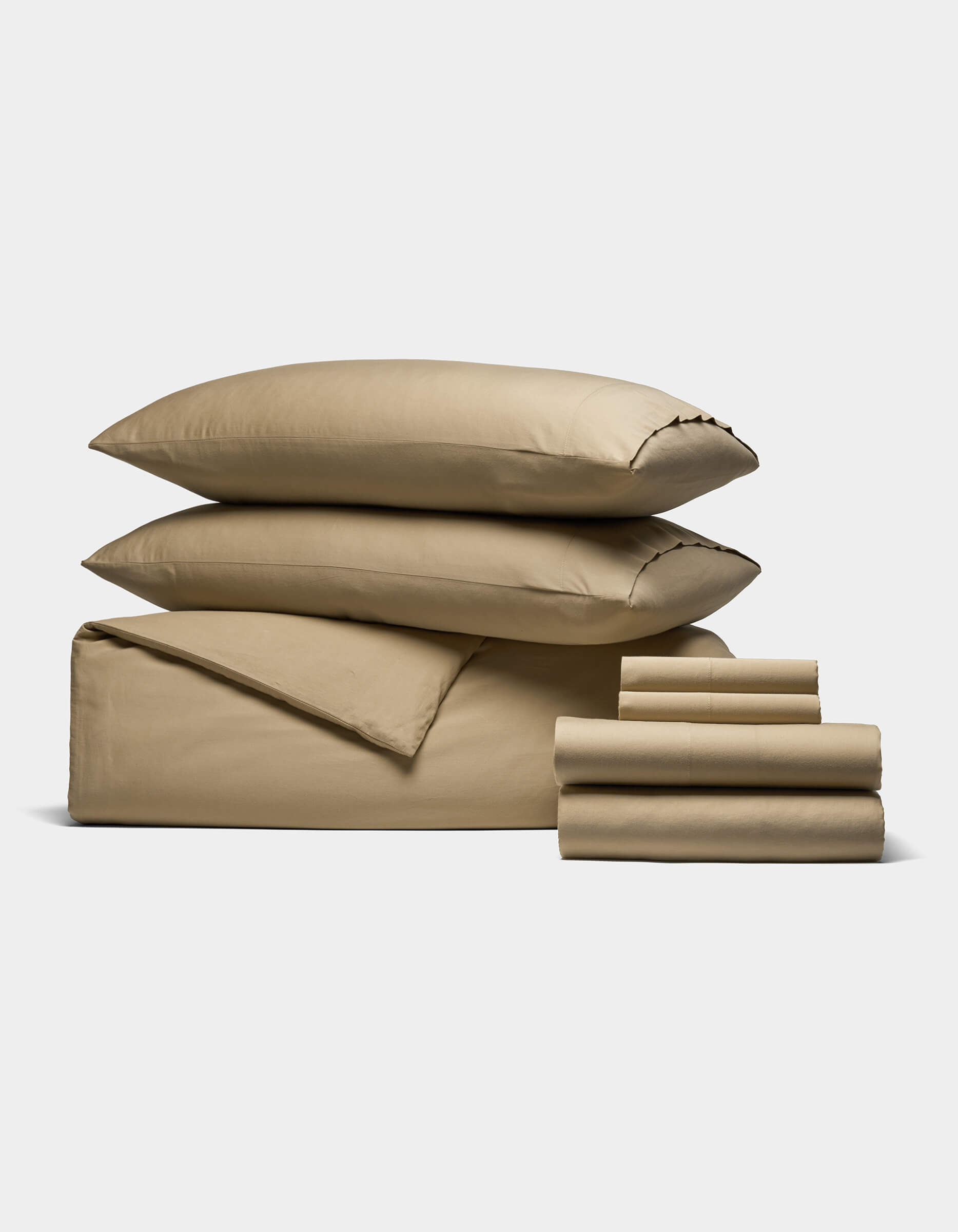 The Soft-Wash Cotton Bedding Core Bundle by Cozy Earth, featuring a tan duvet, flat and fitted sheets, pillowcases, and two stacked pillows, is neatly folded and displayed on a plain white background.|Color:Sandalwood