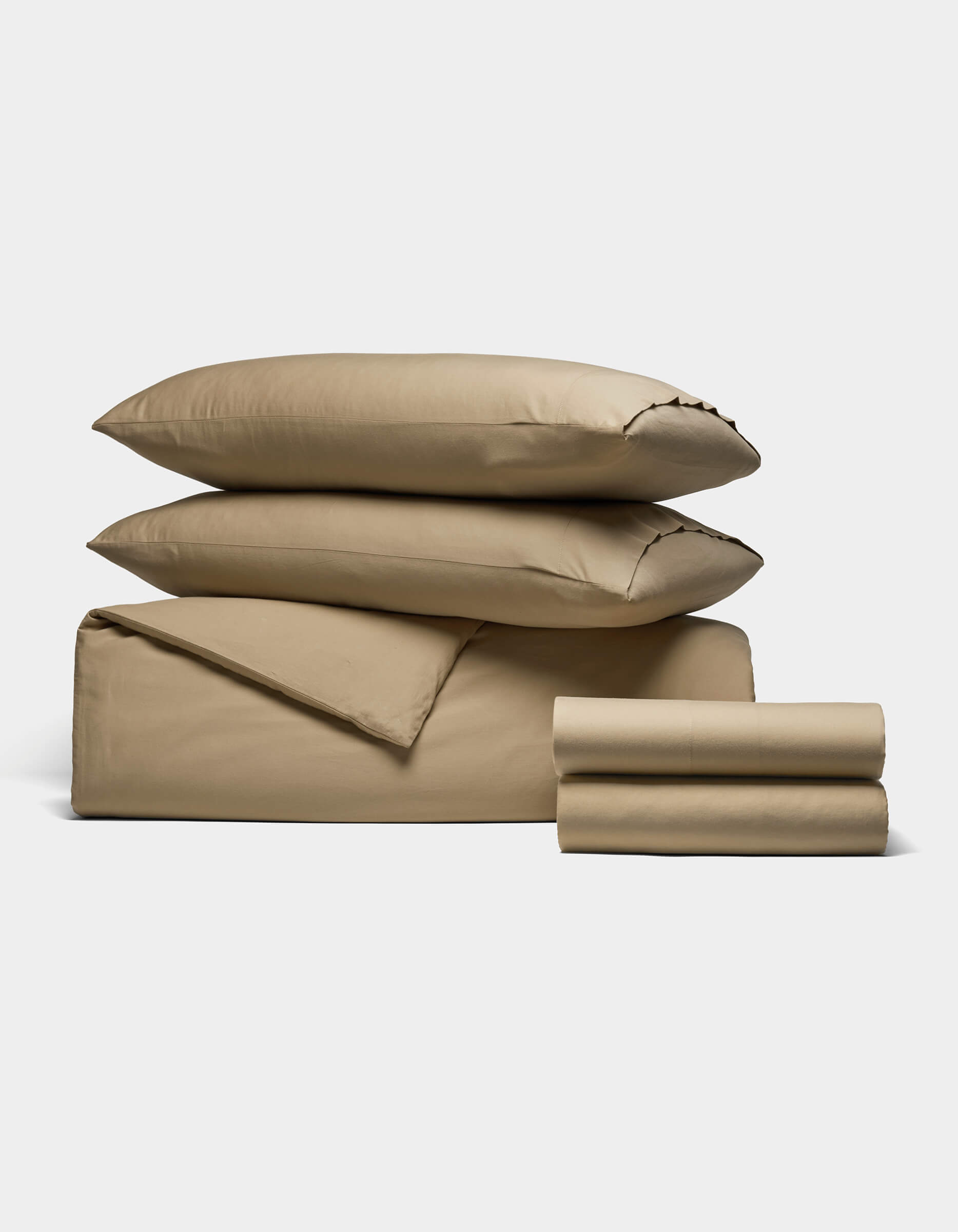The Cozy Earth Soft-Wash Cotton Bedding Deluxe Bundle features two pillows, a folded duvet, and two stacks of tan sheets, all neatly arranged on a white background.|Color:Sandalwood