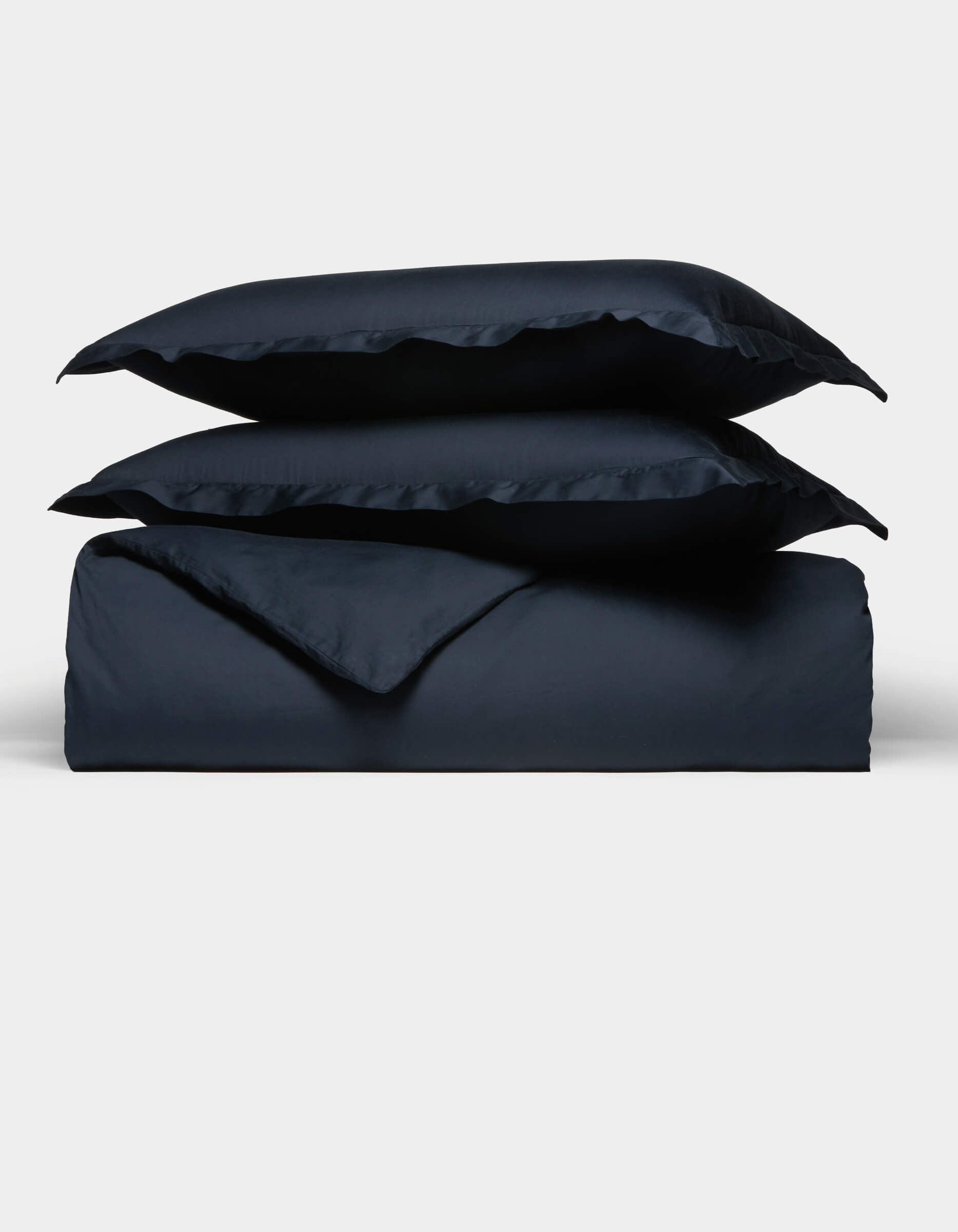 The Cozy Earth Soft-Wash Cotton Duvet Set, in navy blue, features two pillows placed atop a neatly folded duvet, all displayed against a plain white background.