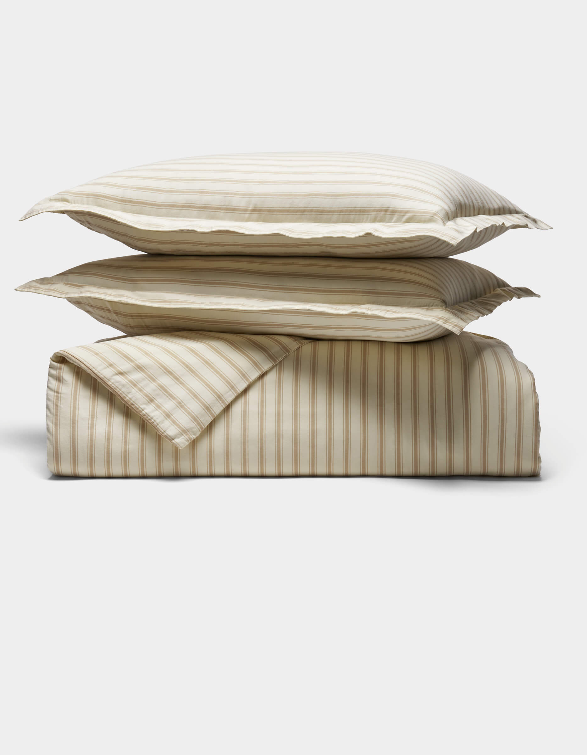 Two striped pillows rest atop a folded matching duvet from the Soft-Wash Cotton Duvet Set by Cozy Earth, all in beige and white tones, set against a plain white background.|Color:Coconut and Sandalwood Stripe