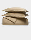 The Cozy Earth Soft-Wash Cotton Duvet Set, featuring two stacked pillows, a folded sheet, and a folded duvet cover in beige, is neatly arranged against a plain white background.|Color:Sandalwood