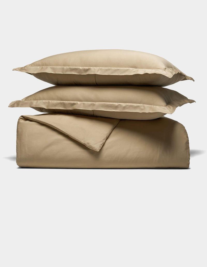 The Cozy Earth Soft-Wash Cotton Duvet Set, featuring two stacked pillows, a folded sheet, and a folded duvet cover in beige, is neatly arranged against a plain white background.