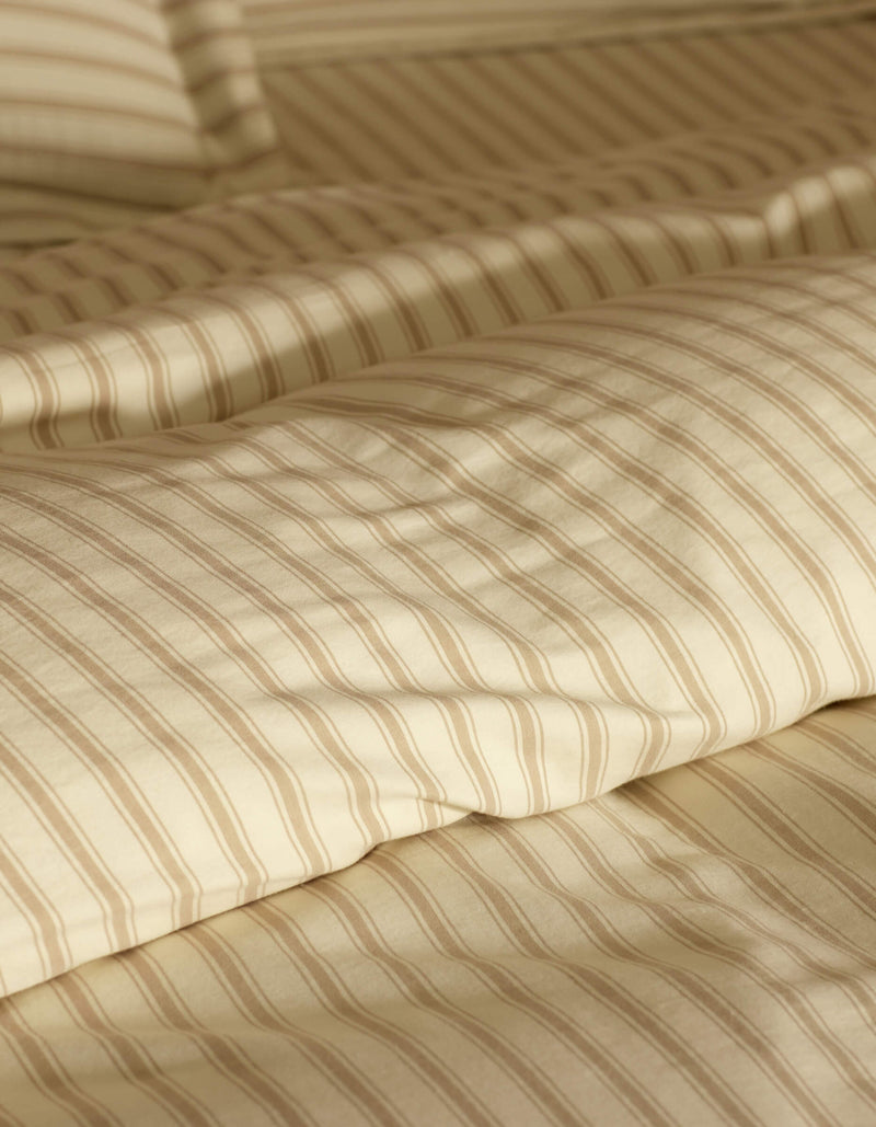 Close-up of a neatly made bed featuring Cozy Earth's Soft-Wash Cotton Duvet Cover in cream and beige stripes, with a matching pillow, softly lit to accentuate the smooth fabric texture.