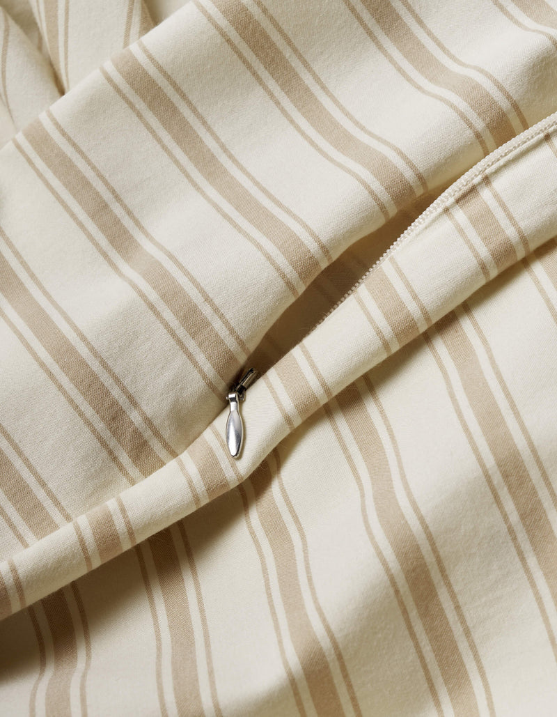 A close-up of the Cozy Earth Soft-Wash Cotton Duvet Cover shows beige and cream vertical stripes, a smooth texture, and a partially open visible zipper.