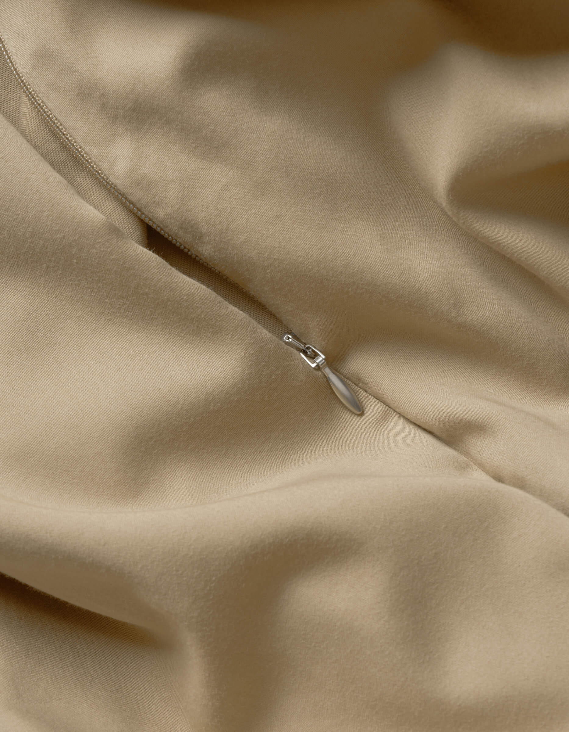 Close-up of Cozy Earth’s Soft-Wash Cotton Duvet Cover in beige, highlighting its smooth texture, soft folds, and a partially closed silver zipper.