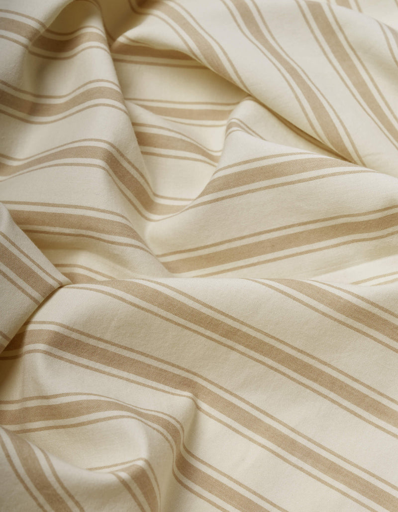 A close-up of Cozy Earth's Soft-Wash Cotton Sheet Set in cream with beige diagonal stripes, softly draped and folded to reveal gentle curves and subtle shadows.