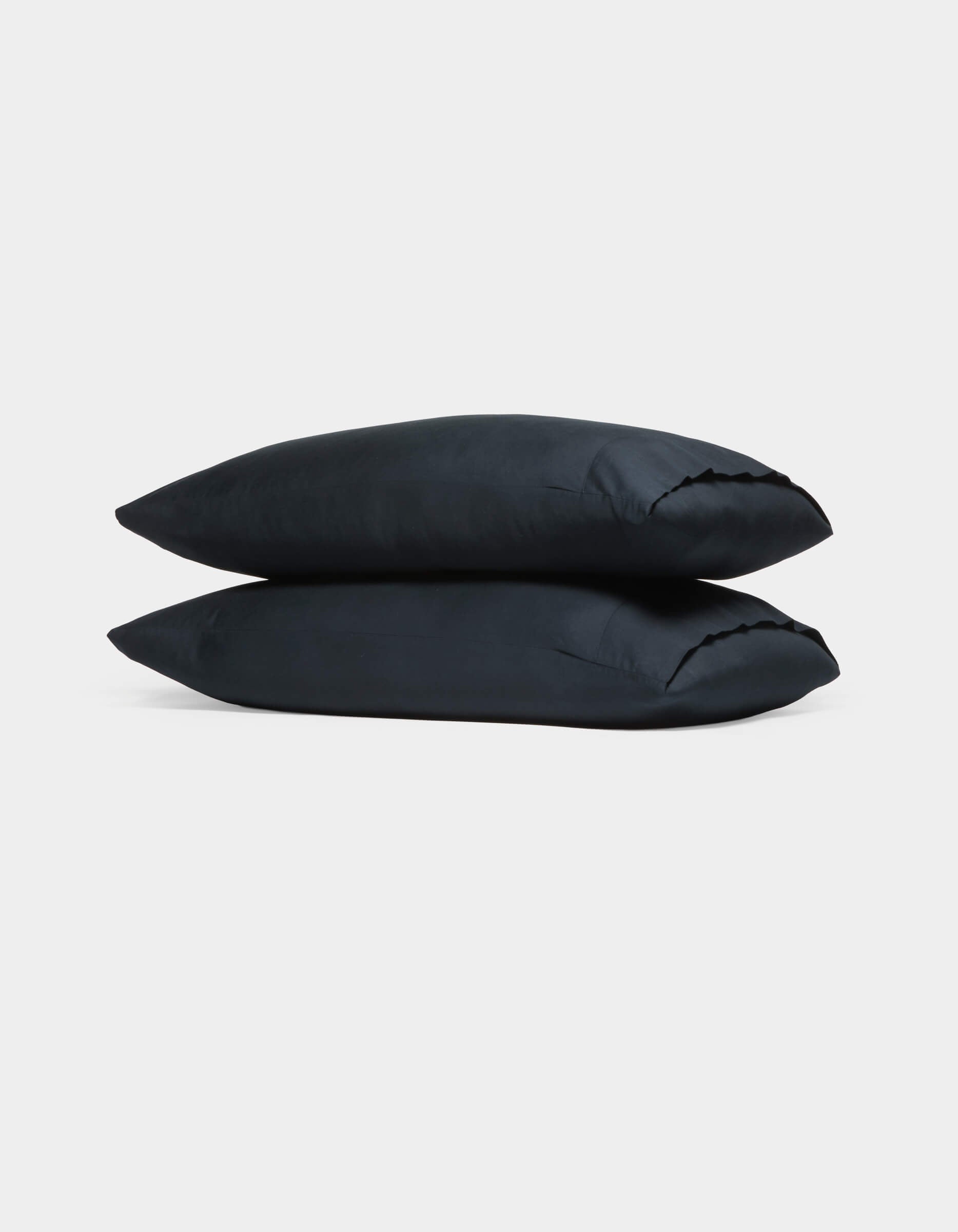 Two Cozy Earth Soft-Wash Cotton Pillowcases in black are stacked atop each other against a plain white background.|Color:Eclipse