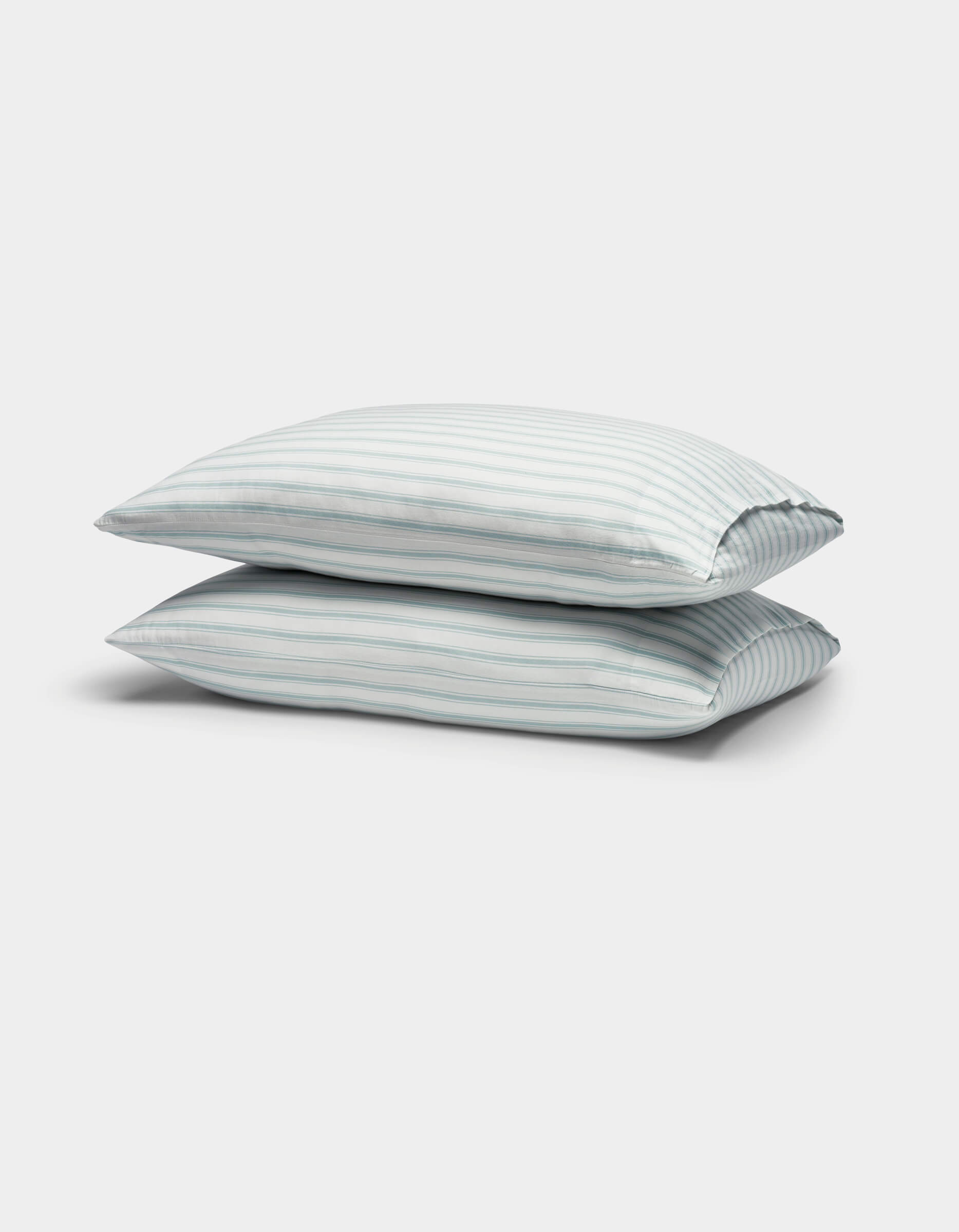 Two Soft-Wash Cotton Pillowcases by Cozy Earth, featuring light blue and white vertical stripes, are stacked against a plain white background.|Color:River and Sea Salt Stripe