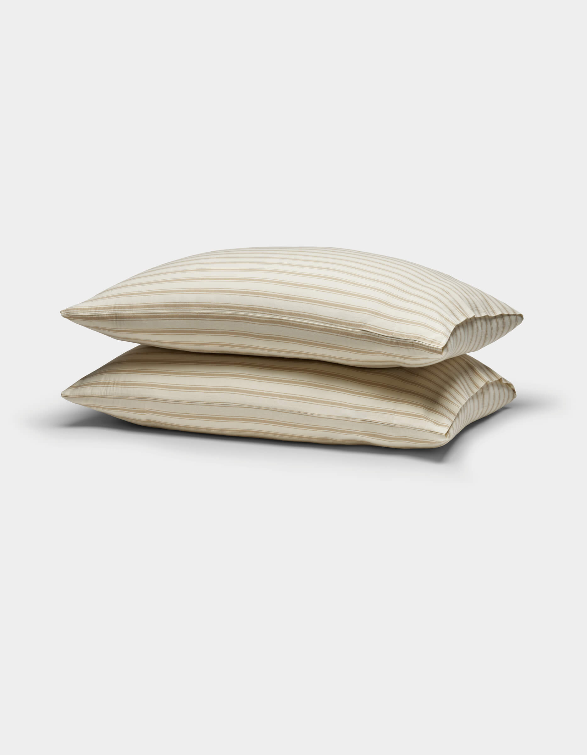 Two Cozy Earth Soft-Wash Cotton Pillowcases in beige with thin horizontal brown stripes are stacked against a plain white background.|Color:Coconut and Sandalwood Stripe