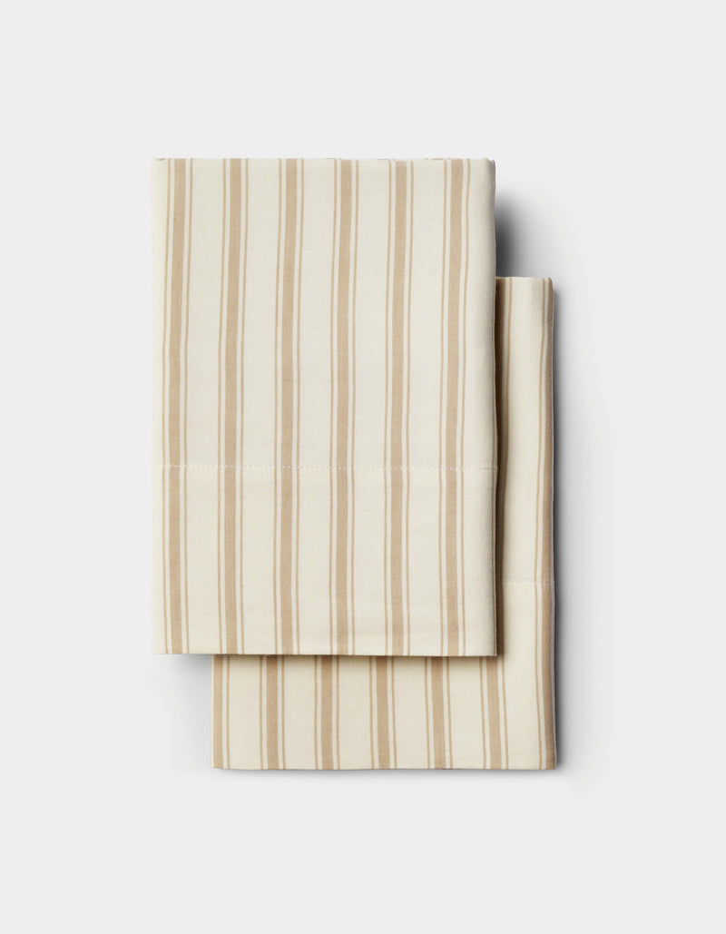 Two folded cream-colored Soft-Wash Cotton Pillowcases by Cozy Earth, featuring thin beige vertical stripes, are stacked neatly on a plain white background.