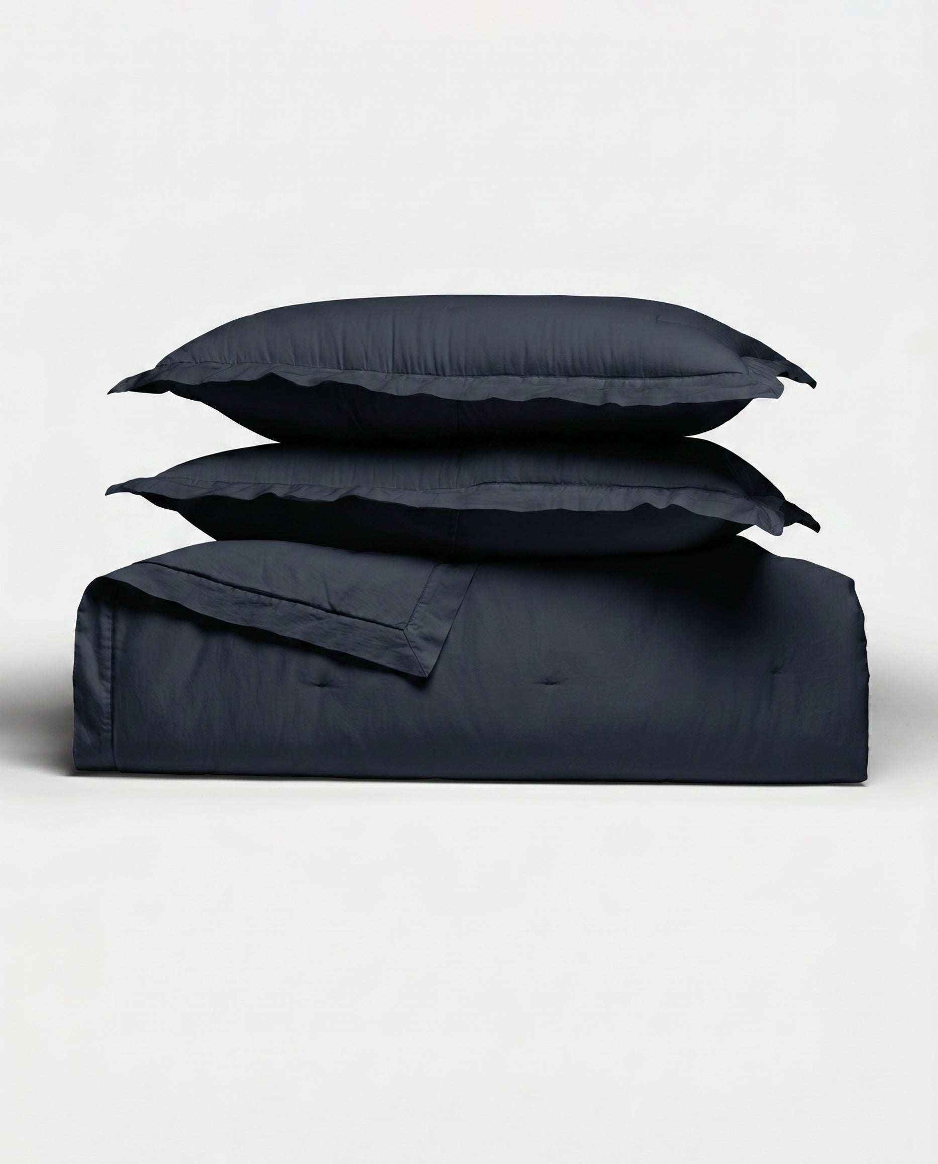 The Cozy Earth Soft-Wash Cotton Quilt Set, featuring a quilt and two pillow shams in dark navy, is neatly stacked against a plain white background.|Color:Eclipse