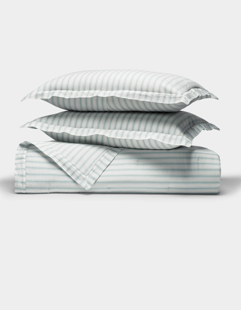 The Cozy Earth Soft-Wash Cotton Quilt Set, featuring two pillows and a folded quilt with light blue and white vertical stripes, is neatly arranged on a white background, highlighting its soft texture.
