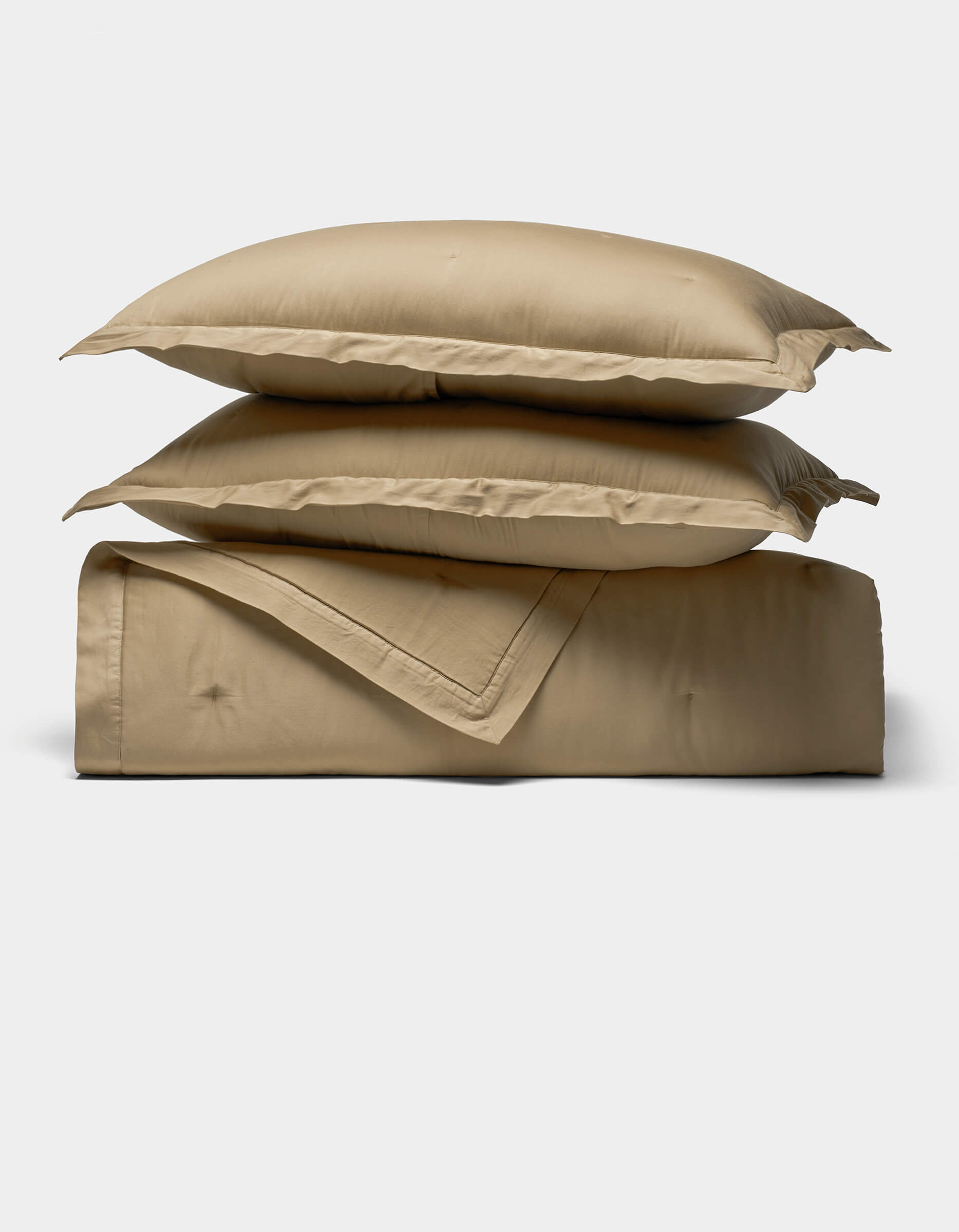 The Soft-Wash Cotton Quilt Set by Cozy Earth features two beige pillows stacked atop a matching folded comforter, displayed against a plain, light background.|Color:Sandalwood