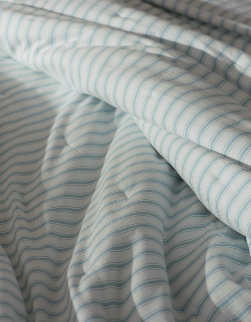 A close-up of the Soft-Wash Cotton Quilt by Cozy Earth, featuring light blue and white stripes on gently wrinkled cotton fabric, softly draped under natural light.