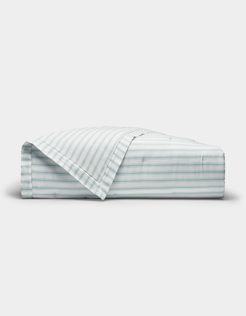 The Cozy Earth Soft-Wash Cotton Quilt is shown neatly folded with one corner turned back, revealing its light color and thin horizontal blue and gray stripes against a plain white background.