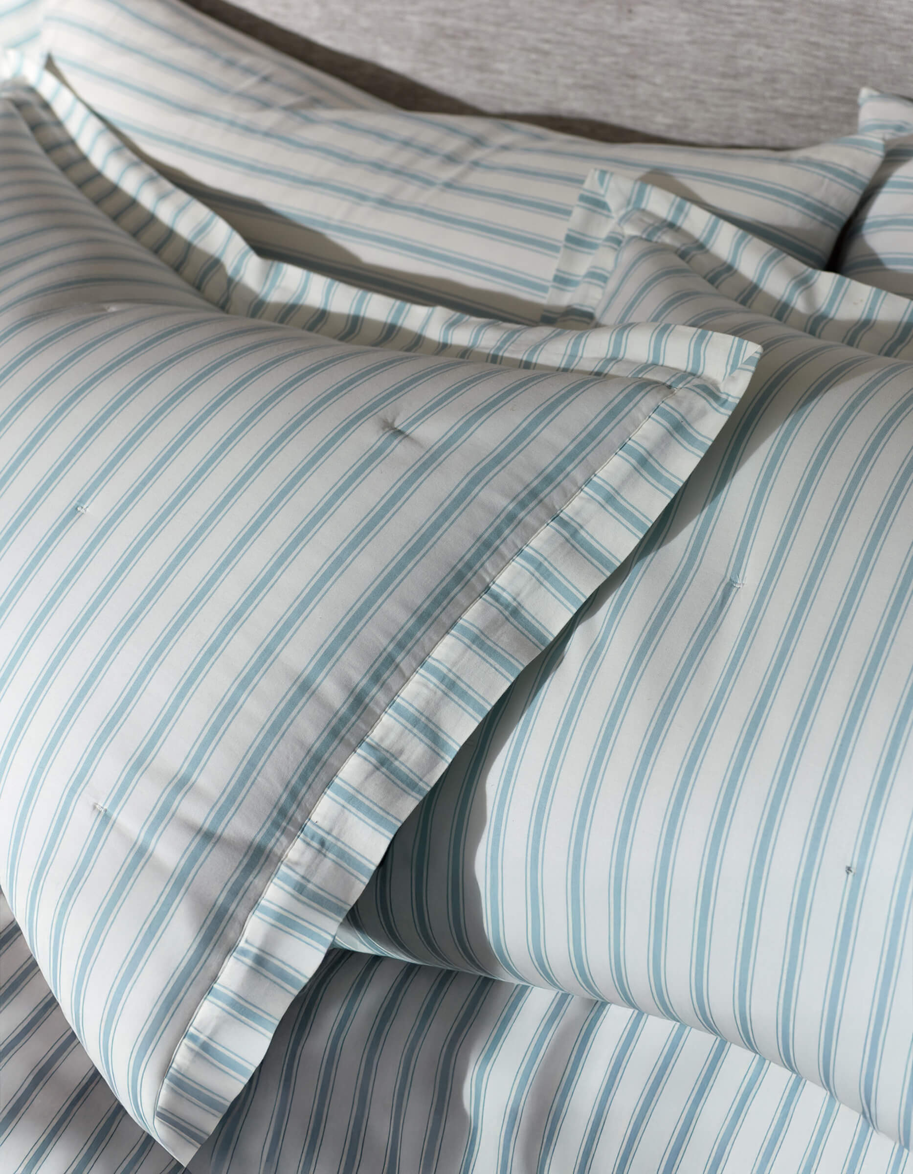 Close-up of Cozy Earth's Soft-Wash Cotton Quilted Shams, neatly arranged with light blue and white vertical stripes, ruffled pillowcase edges, and a soft, textured background.|Color:River and Sea Salt Stripe