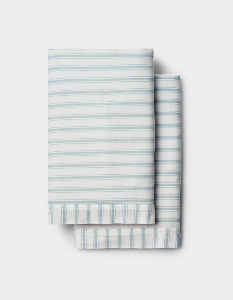 Soft-Wash Cotton Quilted Shams by Cozy Earth in light blue and white stripes are neatly folded and stacked on a white background.